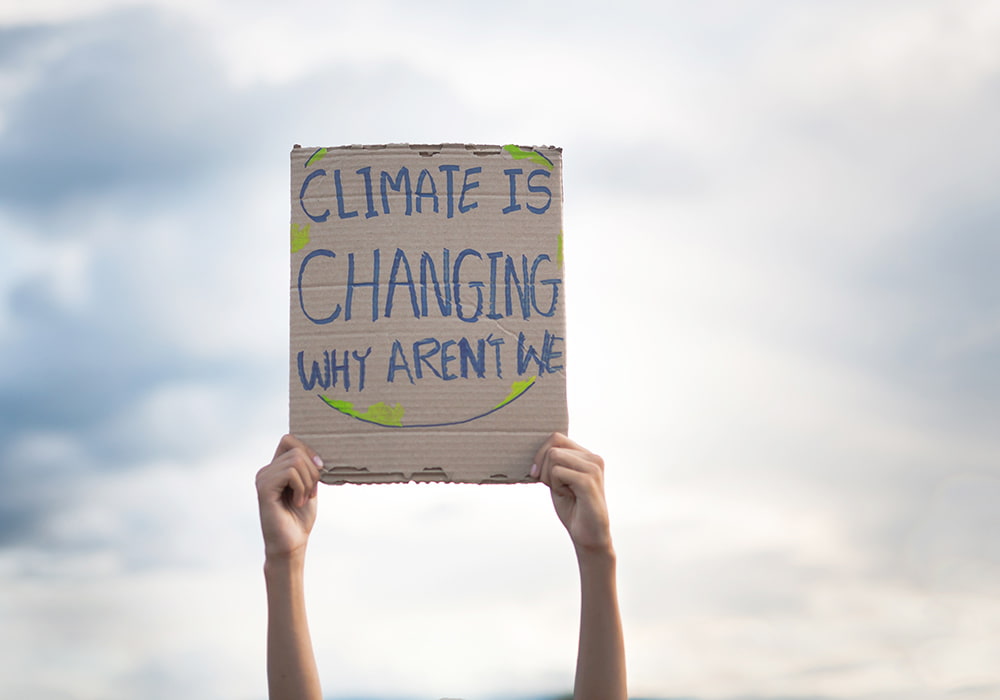 Person Holding Sign: Climate Is Changing Why Aren't We?